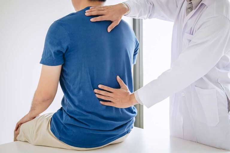 A person sitting on a sofa with one hand on their lower back and a stressed expression on their face.
